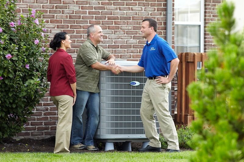 Dealer-HandshakeWithManCouple Degree technician shakes hands with homeowners outside next to AC unit.