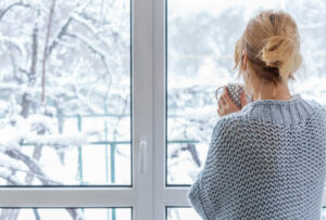 woman in sweater looks outside at winter scene