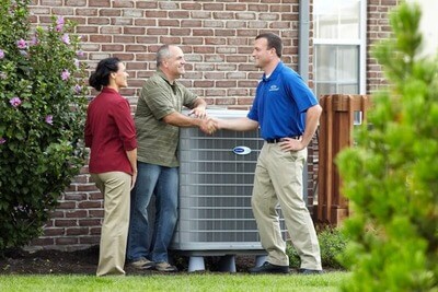 Degree technician shakes hands with homeowners outside next to AC unit.