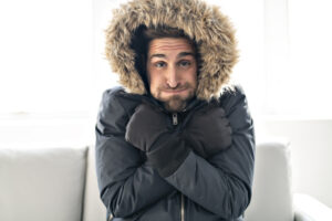 freezing man wearing winter coat sits on sofa
